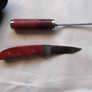 May include: A red and black wood handled knife with a silver blade and a matching red and black wood handled awl.