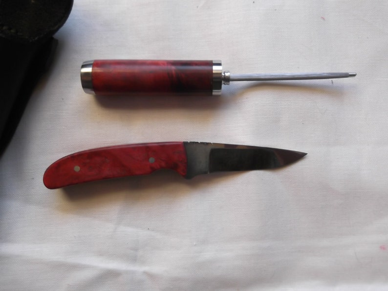 May include: A red and black wood handled knife with a silver blade and a matching red and black wood handled awl.