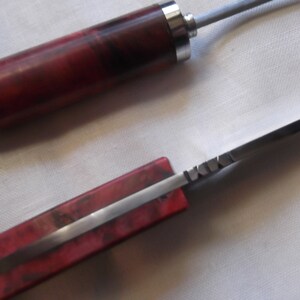 May include: A red and silver pocket knife with a wooden handle. The blade is partially open and the handle has a wood grain pattern.