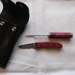 May include: A black leather sheath with two snap closures and a red and silver handled knife with a blade and a small awl.