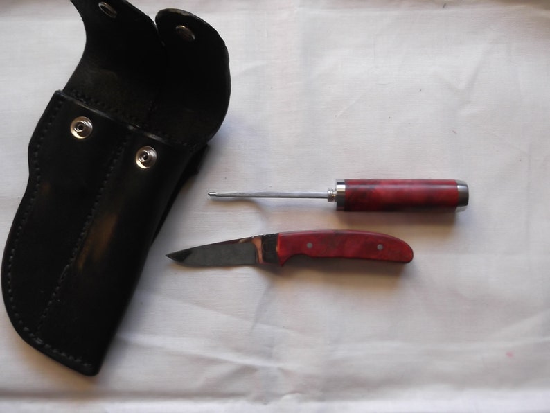 May include: A black leather sheath with two snap closures and a red and silver handled knife with a blade and a small awl.