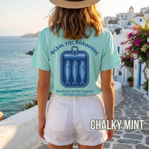 Coastal lifestyle sardine tee inspired by vintage Mediterranean fish markets and classic seafood packaging designs. The bold back print showcases a blue sardine tin illustration with Greek lettering and retro typography for a timeless seaside aesthetic. Printed on a relaxed fit Comfort Colors 1717 t shirt, this design is perfect for summer outfits, Greek travel souvenirs, beach vacations, and seafood inspired fashion lovers.