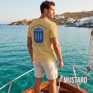 Coastal aesthetic sardine shirt with vintage tinned fish artwork printed on a white Comfort Colors 1717 garment dyed tee. The back print design features three illustrated sardines inside a retro fish tin with Greek lettering and Mediterranean inspired typography. Ideal for seafood lovers, beach aesthetic outfits, Greek island travel fashion, summer vacation clothing, foodie streetwear fans, and anyone who loves nautical inspired graphic tees.