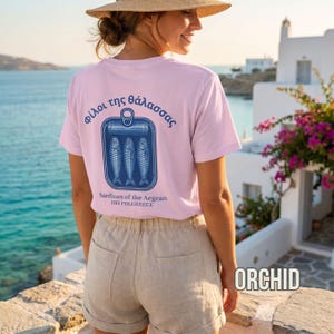 Mediterranean aesthetic graphic tee designed with a vintage sardine can illustration and Greek inspired typography in bold blue print. This relaxed fit Comfort Colors 1717 shirt blends seafood culture with European summer fashion and timeless coastal streetwear style. Ideal for beach lovers, Greek island travelers, foodie apparel fans, nautical graphic tee collectors, and anyone building a coastal aesthetic wardrobe.