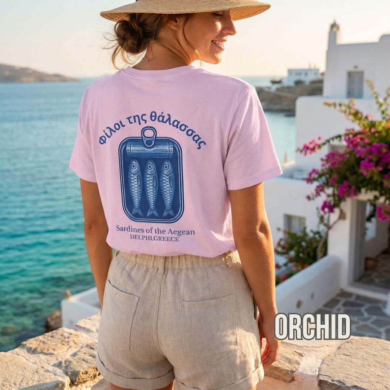 Mediterranean aesthetic graphic tee designed with a vintage sardine can illustration and Greek inspired typography in bold blue print. This relaxed fit Comfort Colors 1717 shirt blends seafood culture with European summer fashion and timeless coastal streetwear style. Ideal for beach lovers, Greek island travelers, foodie apparel fans, nautical graphic tee collectors, and anyone building a coastal aesthetic wardrobe.