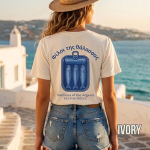 Mediterranean Greece graphic shirt featuring retro sardine can artwork and classic blue coastal print design. This vintage tinned fish tee blends European summer fashion with old world seafood packaging inspiration for a unique coastal aesthetic look. Printed on a Comfort Colors 1717 heavyweight garment dyed t shirt with relaxed fit styling, making it perfect for beach trips, seaside vacations, Greek travel lovers, foodie gifts, and vintage fashion enthusiasts.