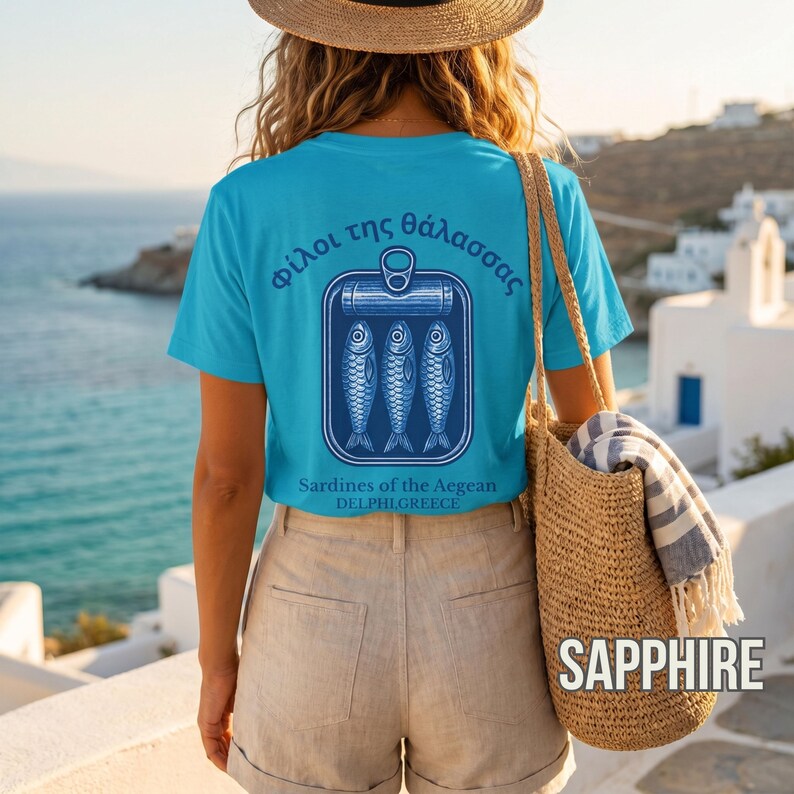 Retro sardine shirt inspired by Mediterranean seafood culture and coastal European summer fashion. The oversized back graphic displays a vintage style sardine tin illustration with Greek text and “Sardines of the Aegean” typography in blue ink on a white Comfort Colors 1717 t shirt. Great for coastal lifestyle outfits, tinned fish aesthetic fans, nautical fashion lovers, Greek vacation souvenirs, and unique foodie apparel collections.