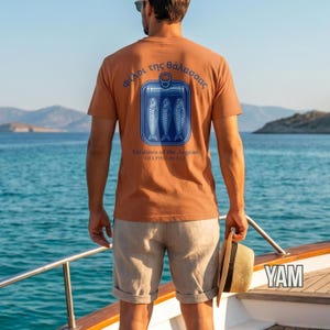 Vintage tinned fish shirt with Mediterranean Greece inspired artwork featuring three sardines inside a retro can graphic. The nautical blue print and Greek typography create a unique coastal aesthetic look perfect for beach town fashion, European summer outfits, foodie gifts, and relaxed streetwear styling. Printed on a premium Comfort Colors 1717 garment dyed t shirt with heavyweight cotton comfort and timeless vintage appeal.