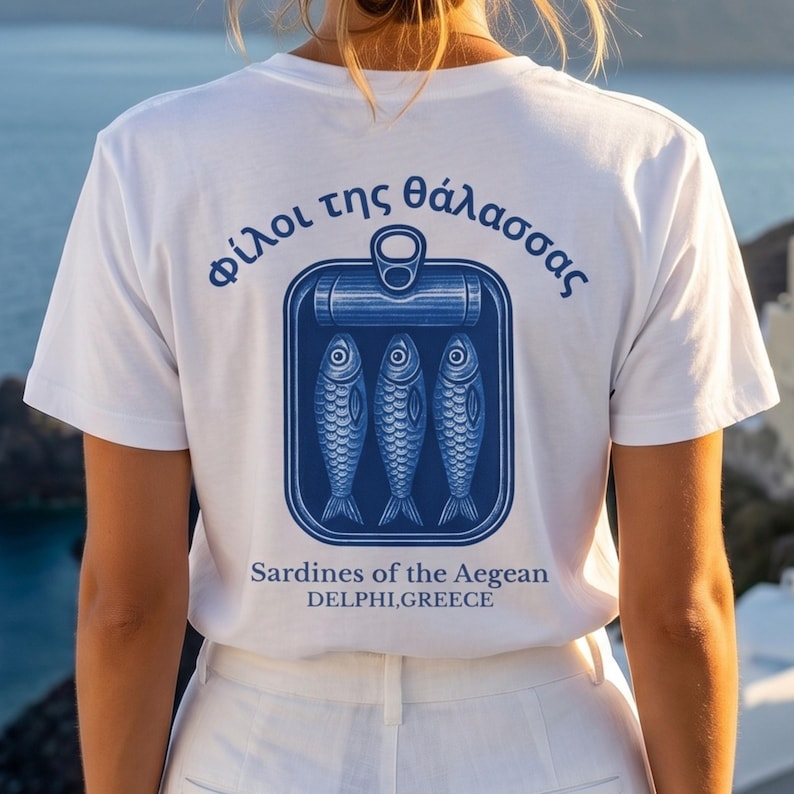 Mediterranean Greece graphic shirt featuring retro sardine can artwork and classic blue coastal print design. This vintage tinned fish tee blends European summer fashion with old world seafood packaging inspiration for a unique coastal aesthetic look. Printed on a Comfort Colors 1717 heavyweight garment dyed t shirt with relaxed fit styling, making it perfect for beach trips, seaside vacations, Greek travel lovers, foodie gifts, and vintage fashion enthusiasts.