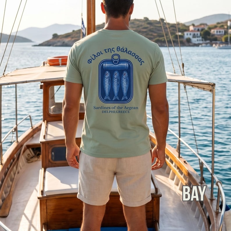 Vintage coastal graphic tee with detailed sardine can artwork inspired by Greece and Mediterranean beach culture. This tinned fish shirt features bold blue nautical style graphics and retro seafood packaging aesthetics printed on a premium Comfort Colors 1717 garment dyed shirt. A perfect choice for coastal fashion lovers, summer travel outfits, retro streetwear styling, beach town aesthetics, seafood enthusiasts, and relaxed everyday casual looks.