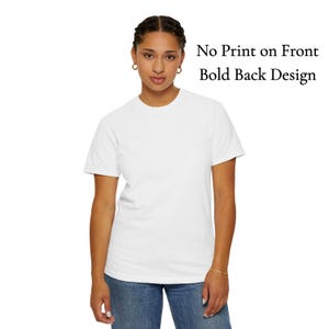 May include: A white crew neck t-shirt with the text "No Print on Front Bold Back Design". The shirt is worn with blue jeans. The model is wearing gold hoop earrings and a gold bracelet.