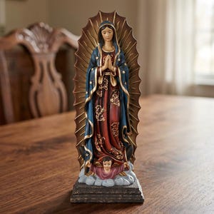 May include: A standing figurine of Our Lady of Guadalupe featuring a dark blue mantle with gold stars over a deep red dress with gold floral patterns. The figure is framed by a brown sunburst halo and stands on a base with a small angel figure.