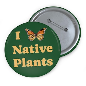May include: A green button with the text "I Native Plants" in a light orange color. A monarch butterfly is above the text. The back of the button is silver.