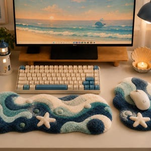 May include: A mechanical keyboard with white and blue keycaps, a tufted fabric keyboard wrist rest, and a matching mouse pad featuring a wavy ocean pattern with white starfish accents. A white computer mouse sits on the tufted mouse pad.