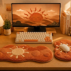 May include: A computer desk setup featuring a white and orange mechanical keyboard, a white computer mouse, and two textured, cloud-shaped desk mats in shades of orange and cream, each decorated with a raised sun motif on a wooden surface.