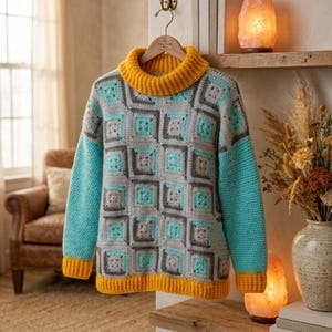 May include: A handmade crochet sweater with a geometric pattern. The sweater features a gray body with turquoise and gray squares, turquoise sleeves, and a yellow turtleneck and trim. The sweater is hanging on a wooden hanger.