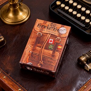 May include: A tarot card deck box with a brown leather backpack design. The box features the text "Broke Bi Tarot Training Deck" and includes patches of a Canadian flag, a green patch, and a Spanish flag. The box is on a brown leather surface.