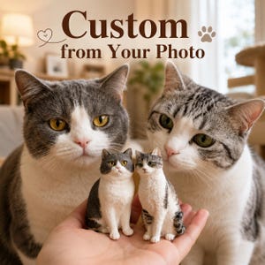 Puede incluir: Dos pequeñas figuras de gato, una gris y blanca y otra atigrada y blanca, sostenidas en una palma. El texto Custom from Your Photo aparece arriba con un icono de corazón y huella. Las figuras se parecen a los dos gatos del fondo.