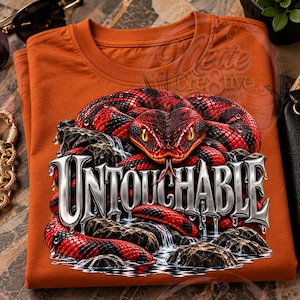 May include: A burnt orange t-shirt featuring a graphic of a red and black snake coiled over dark rocks with water flowing around them. The word UNTOUCHABLE is printed in large, metallic, silver-toned letters across the centre of the design.
