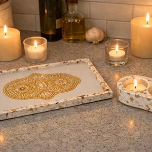 May include: A decorative arrangement featuring lit candles and a tray. The tray has a white surface with a gold design. Two pillar candles, votive candles, and a double candle holder are also lit, creating a warm ambiance.