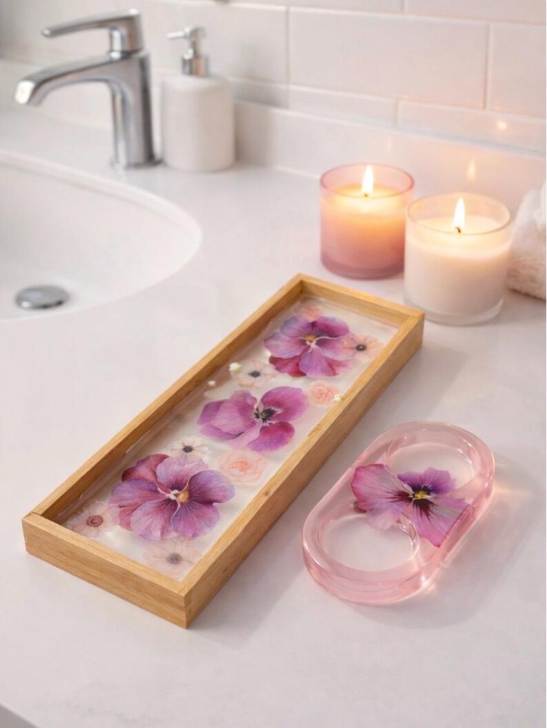 May include: A rectangular wooden tray with a clear resin base containing pressed purple pansies and small white flowers, alongside a matching oval-shaped pink resin ring holder featuring a single pressed purple pansy embedded inside.
