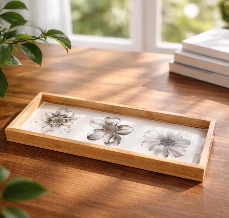 May include: A rectangular wooden tray with a light brown finish and a white base. The interior of the tray features a decorative print of three distinct black and white floral illustrations arranged in a horizontal line across the center.