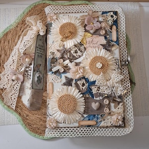 Könnte beinhalten: Ein dekoratives Journal mit cremefarbener Spitzenborte, drei großen Bast-Sonnenblumen, Stoffresten, Holzknöpfen und einem Anhänger mit dem Text "Find yourself". Das Journal ist mit kleinen Stoffblumen, einem Herzanhänger und Spitzenband verziert.