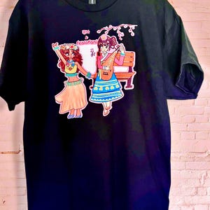 Puede incluir: Una camiseta negra de manga corta con un estampado gráfico de dos figuras. Una figura lleva un conjunto de estilo hula con un collar de flores, mientras que la otra lleva un hanbok tradicional y toca un instrumento de cuerda. El texto dice "평화" y "fealofani".