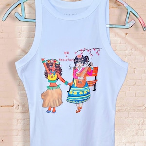 Puede incluir: Una camiseta sin mangas blanca con un estampado gráfico colorido de dos figuras tomadas de la mano. Una figura lleva una falda hula y un collar de flores, mientras que la otra viste un hanbok tradicional y toca un instrumento. Texto: 평화 & fealofani.