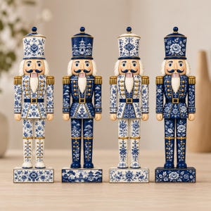 Può includere: Quattro statuette di schiaccianoci in piedi disposte in fila. Ogni figura indossa un cappello alto e un'uniforme decorata con motivi floreali blu e bianchi, dettagli dorati e una barba bianca. Le basi sono rettangolari con disegni floreali.