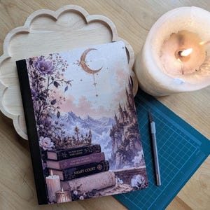 Peut inclure: Un livre à couverture rigide avec une illustration fantastique représentant un croissant de lune, des montagnes, un château et une pile de livres avec le texte To The Stars Who Listen, And The Dreams That Are Answered, Night Court et ACOTAR.