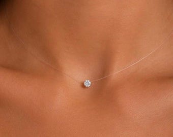 Op de afbeelding: Een ketting van een dunne, transparante nylondraad met een enkele, kleine, ronde, wit geslepen edelsteen als hanger, gecentreerd aan de basis van de nek. Het doorzichtige koord creëert een zwevend effect voor de fonkelende, gefacetteerde steen.