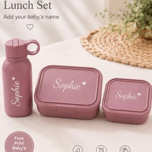 Puede incluir: Un set de almuerzo color malva que incluye una botella de agua y dos recipientes rectangulares, cada uno personalizado con el nombre Sophie y un corazón. Texto: Personalized Lunch Set, Add your baby's name, Free Print Baby's Name, BPA Free, Food Grade, Easy to Clean.