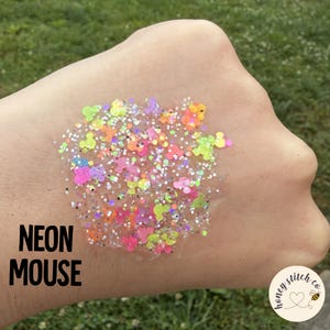 May include: A collection of neon-colored glitter in a clear gel base, featuring small mouse-shaped sequins in pink, orange, yellow, and green, mixed with silver holographic sparkles. The text NEON MOUSE is printed in black on the left side.
