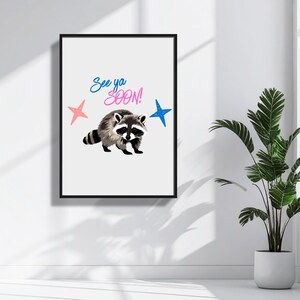 May include: A framed art print featuring a raccoon illustration with the text "See ya SOON!" in blue and pink. The artwork includes pink and blue star accents, set against a white background.
