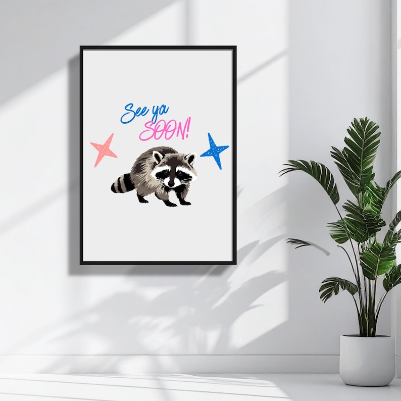 May include: A framed art print featuring a raccoon illustration with the text "See ya SOON!" in blue and pink. The artwork includes pink and blue star accents, set against a white background.