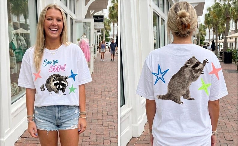 May include: White t-shirt with a raccoon graphic and the text "See ya SOON!" on the front. The back of the shirt features a raccoon and star graphics. The shirt is a casual, everyday wear item.