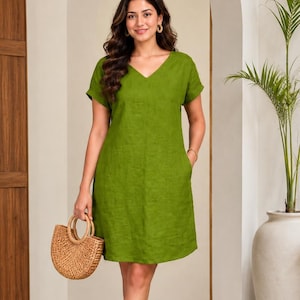 May include: A knee-length, grass-green dress with short sleeves and a V-neckline. The dress features a simple, straight-cut silhouette and is paired with a round, woven straw handbag and light-colored slide sandals, creating a cohesive look.