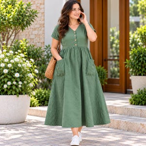 May include: A sage green midi dress featuring a V-neckline, short sleeves, and a button-down front bodice. The dress includes two large patch pockets on the front skirt and a gathered waistline, paired with a brown woven shoulder bag.