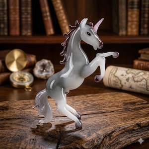 May include: A glass unicorn figurine in a rearing pose. The unicorn has a gray body with a pink horn and dark red mane and hooves. The figurine is displayed on a wooden surface.