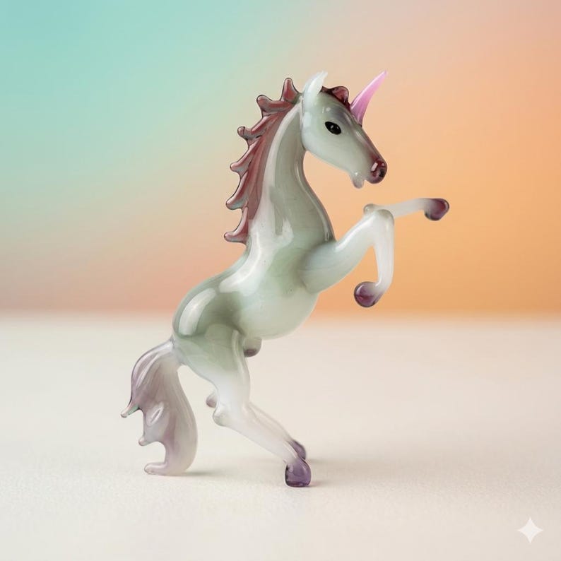 May include: A glass unicorn figurine in a rearing pose. The unicorn has a white body with subtle green and purple accents. Its mane and tail are a deep burgundy, and it has a pink horn. The figurine is set against a soft, gradient background.