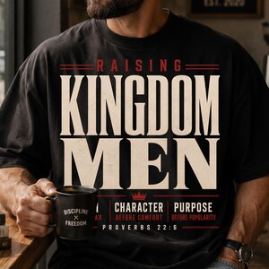 May include: A black short-sleeved t-shirt featuring the white and red text RAISING KINGDOM MEN, with additional text including CHARACTER BEFORE COMFORT, PURPOSE BEFORE POPULARITY, and PROVERBS 22:6 printed on the front in a bold, graphic design.