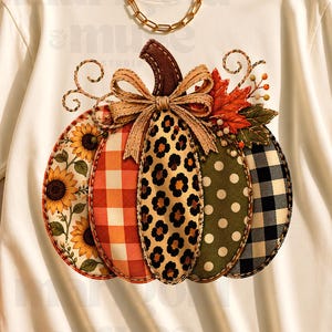 May include: A cream-coloured short-sleeve t-shirt featuring a large central graphic of a pumpkin composed of five distinct vertical segments with sunflower, orange plaid, leopard print, green polka dot, and black buffalo check patterns.