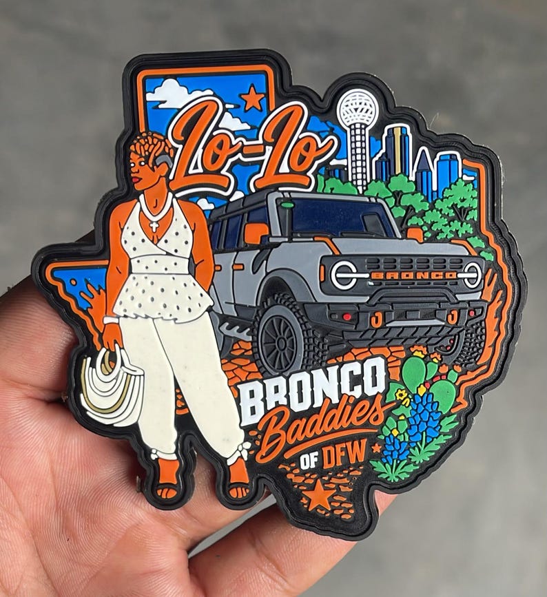 May include: A rubber patch shaped like Texas featuring a gray SUV, a person in a white polka-dot top and pants holding a white bag, and the text Lo-Lo, BRONCO Baddies OF DFW. The design includes a city skyline, blue sky, orange stars, and green cacti.