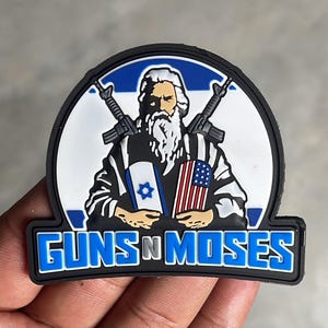 May include: A semi-circular PVC patch featuring a bearded figure holding an Israeli flag and an American flag, with two rifles crossed behind them. The text GUNS N MOSES is printed in bold blue letters at the bottom against a black border.