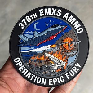 May include: A circular morale patch featuring a dark blue night sky with a crescent moon and stars above a military jet firing a missile. Below, a ground-based missile launcher is engulfed in flames. Text reads 378TH EMXS AMMO OPERATION EPIC FURY.