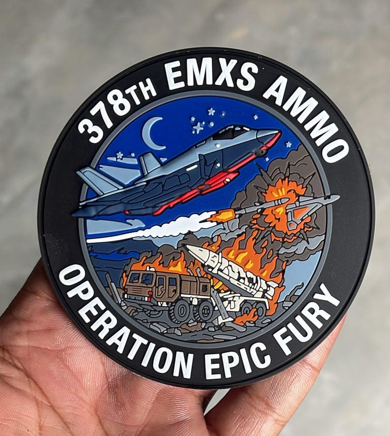 May include: A circular morale patch featuring a dark blue night sky with a crescent moon and stars above a military jet firing a missile. Below, a ground-based missile launcher is engulfed in flames. Text reads 378TH EMXS AMMO OPERATION EPIC FURY.