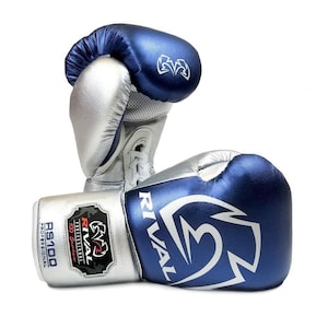 Könnte beinhalten: Paar blaue und silberne Boxhandschuhe. Auf den Handschuhen ist der Markenname "RIVAL" aufgedruckt. Die Handschuhe sind aus Leder und haben einen Schnürverschluss. Die Handschuhe sind für den professionellen Gebrauch konzipiert.