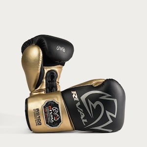 Könnte beinhalten: Ein Paar schwarze und goldene Sparringshandschuhe mit dem Text Rival, RS100 und Professional 100 Series. Die Handschuhe haben ein markantes Logo an der Seite, ein Klettverschlusssystem am Handgelenk und ein metallisches Gold-Finish am Daumen.