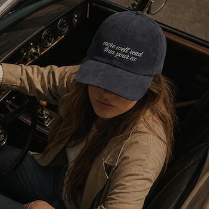 May include: A navy blue baseball cap featuring the embroidered white text "more well read than your ex" on the front panel. The cap has a structured crown, a curved brim, and is made of a corduroy fabric with a visible ribbed texture.